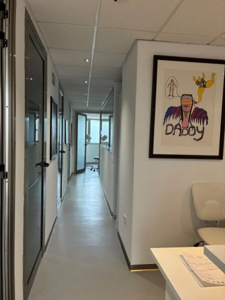 Heller Flur mit Kunstwerken - führt zu den Behandlungsräumen, dem Eingriffsraum und dem Sprechzimmer der Inselproktologie Mallorca.